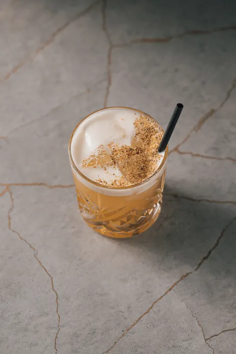 Un cocktail ambré à la mousse épaisse, servi sur glace