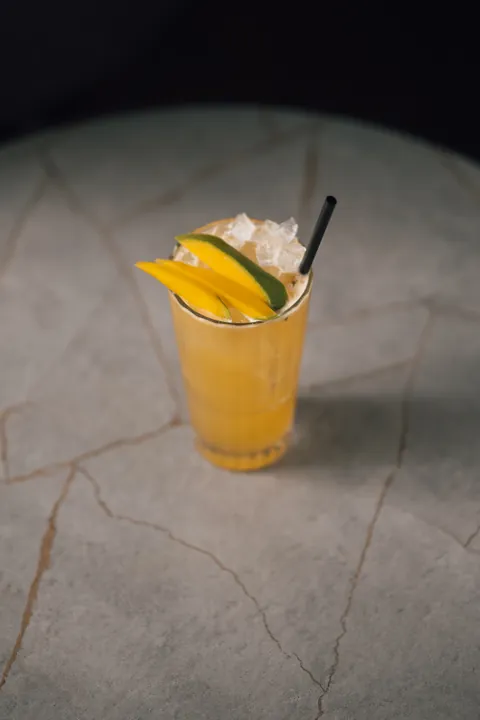 Un cocktail jaune sur glace pilée, tranches de mangue et citron vert