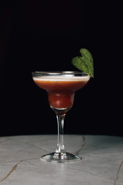 Un cocktail rouge sombre servi en verre à pied, feuille de menthe