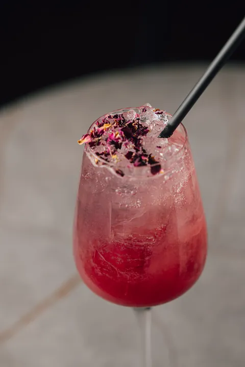 Un cocktail rose sur glace pilée, pétales de fleurs séchées