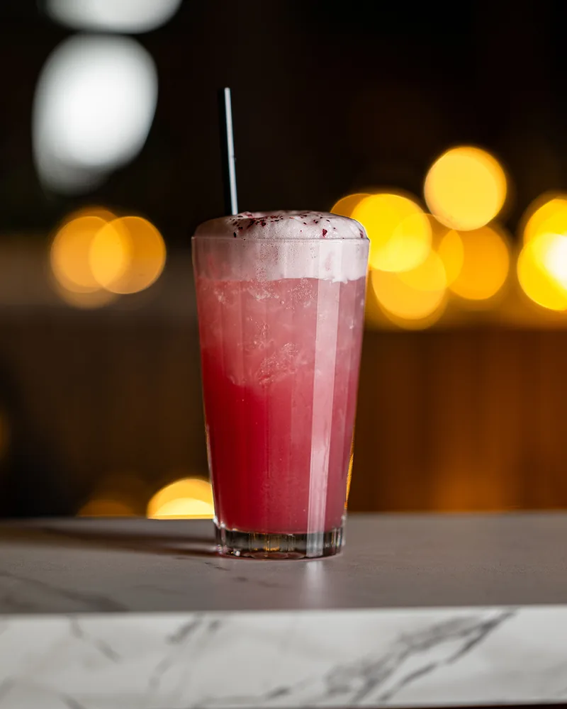 Un cocktail rose sous une mousse légère, servi sur le comptoir