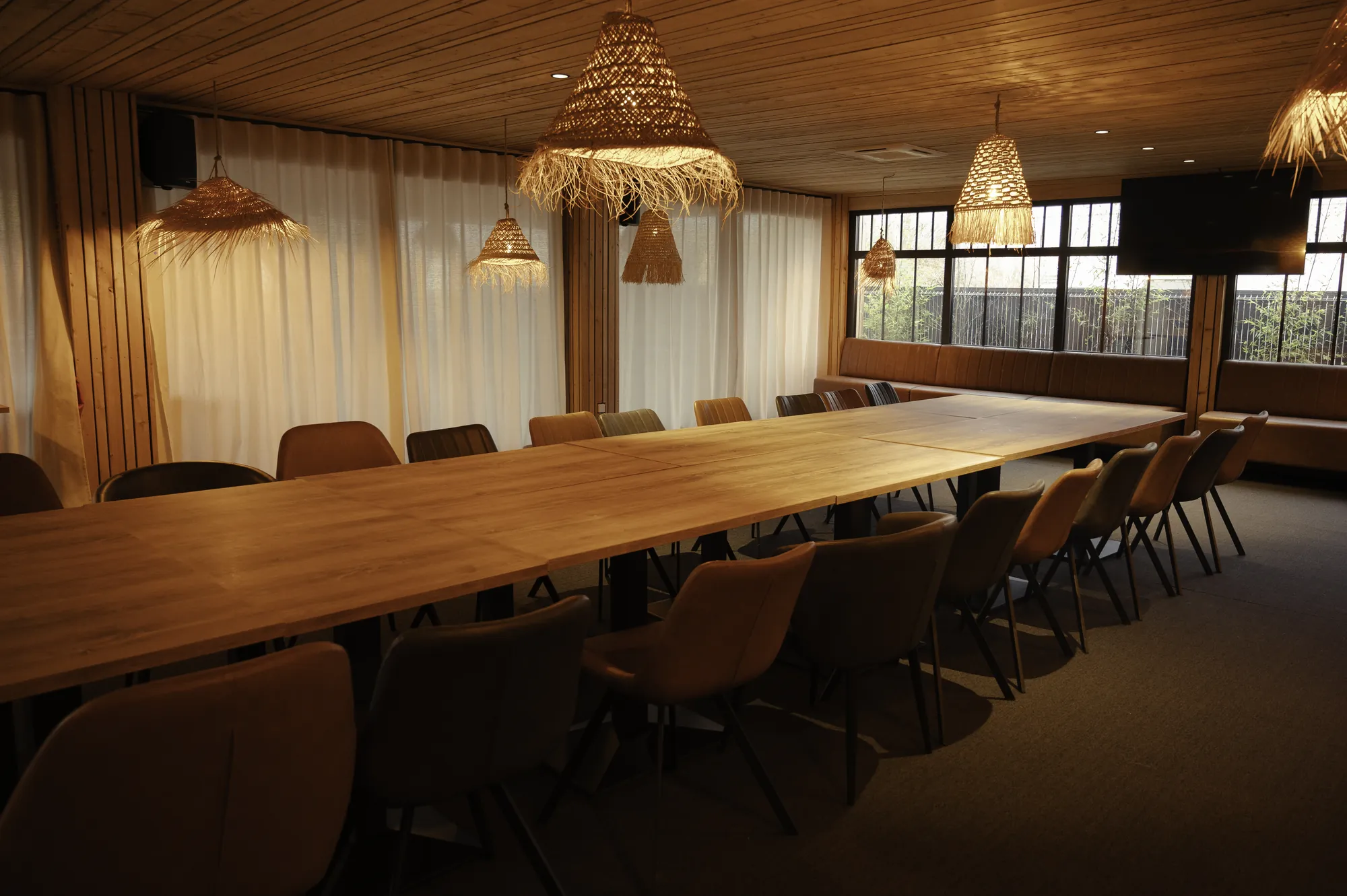 La salle dressée pour un repas de groupe, une grande tablée sous les suspensions